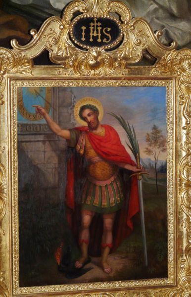 Expeditus met in de linkerhand de palmtak van het martelaarschap; met de rechter wijst hij op klok (zonnewijzer); onder de klok: 'Hodie' ('vandaag nog').