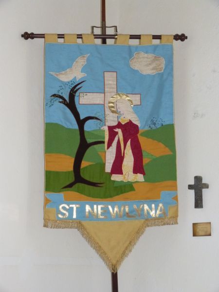DE ontwerper van het processievaandel maakt Saint Newlina tot een kluizenares die een nieuwe boom heeft uitgezaaid en vervolgens met haar zorgen omringt: symbool voor het evangekie dat zij wellicht bracht in de streken rond Newlyn-East? Ca 2000, processievaandel.