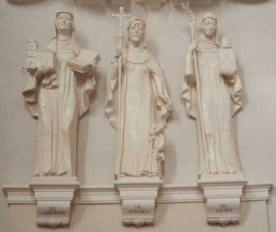Lioba (rechts) als benedictines met staf, boek en klok. Naast haar in het midden haar gezellin Thecla; (helemaal links Geertruida van Helfta). Wandskulptuur in het priesterkoor van de Domkerk te Mainz, 2e helft 20e eeuw. Eigen foto.