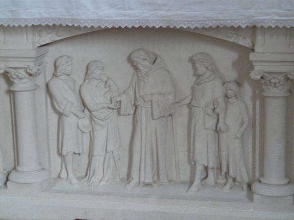 Viaud doet de plaatselijke bevolking delen in zijn zegeningen en weldaden. Ca 1900, sculptuur, altaarvoet.