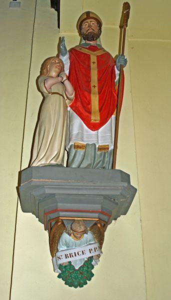 Livinus in gezelschap van Brictius. Curieus dat de ondertitel van het beeld niet verwijst naar de bisschop, maar naar de 'jongen' naast hem. Er is weliswaar een bisschop Brictius (van Tours: 13 november), maar die wordt nooit afgebeeld met een opgroeiende jongen naast zich. Ca 1935(?), sculptuur [Met dank aan Vic Van Cutsem]